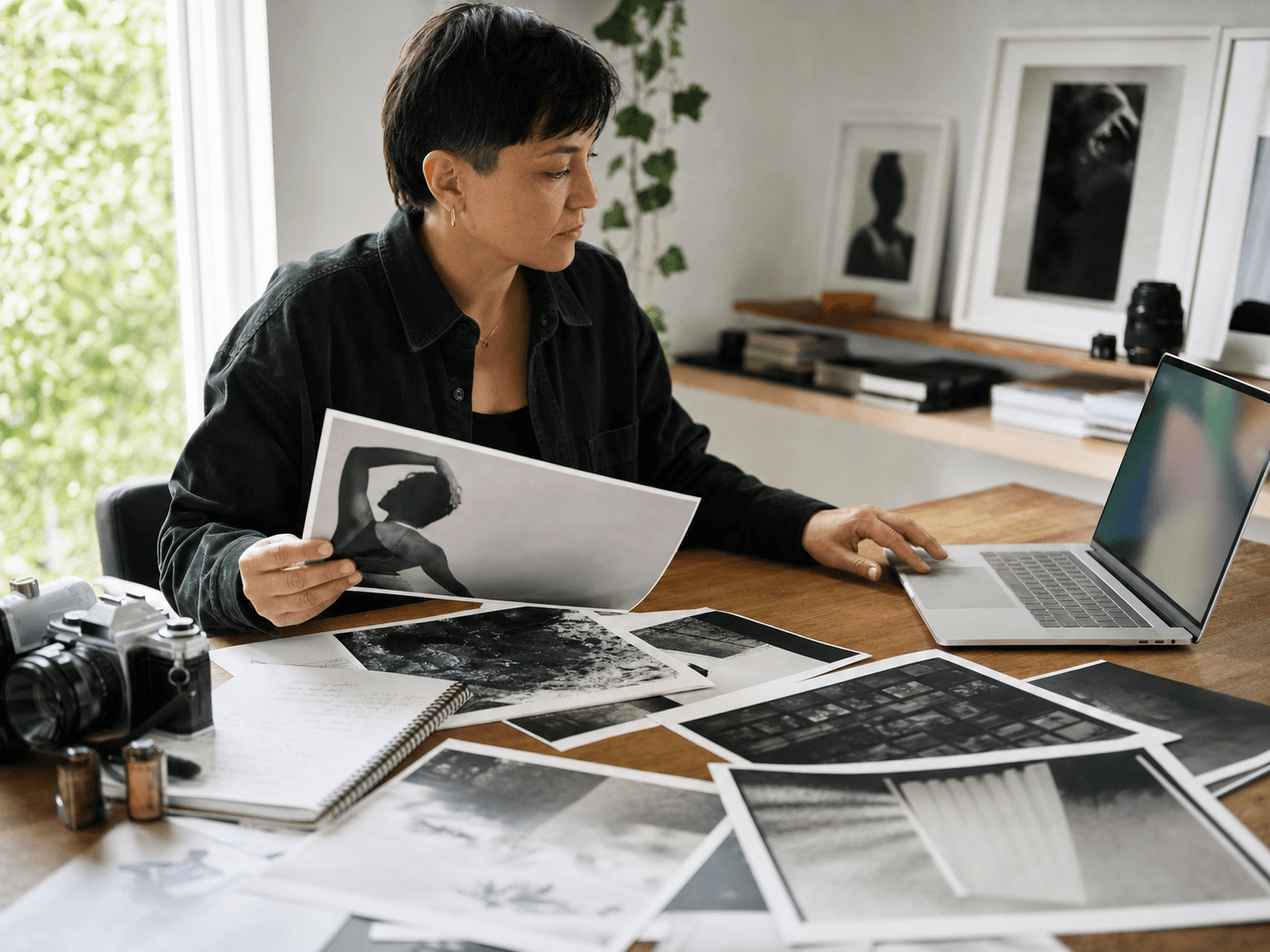 Photographer selecting prints beside a laptop in a working studio